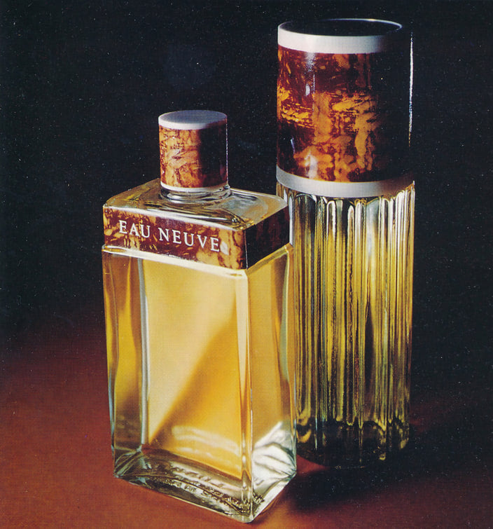Photographie publicitaire en couleur de deux flacons d'Eau Neuve en verre ambré, l'un rectangulaire portant l'inscription « Eau Neuve », l'autre cylindrique et cannelé, coiffés de bouchons façon écaille, sur fond rouge sombre.