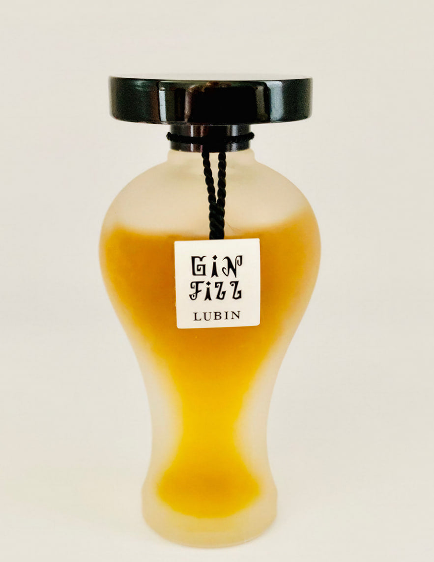 Le flacon de Gin Fizz, en verre dépoli de forme balustre, surmonté d'un large bouchon noir laqué, avec une étiquette carrée portant « Gin Fizz Lubin » suspendue par un cordon noir.