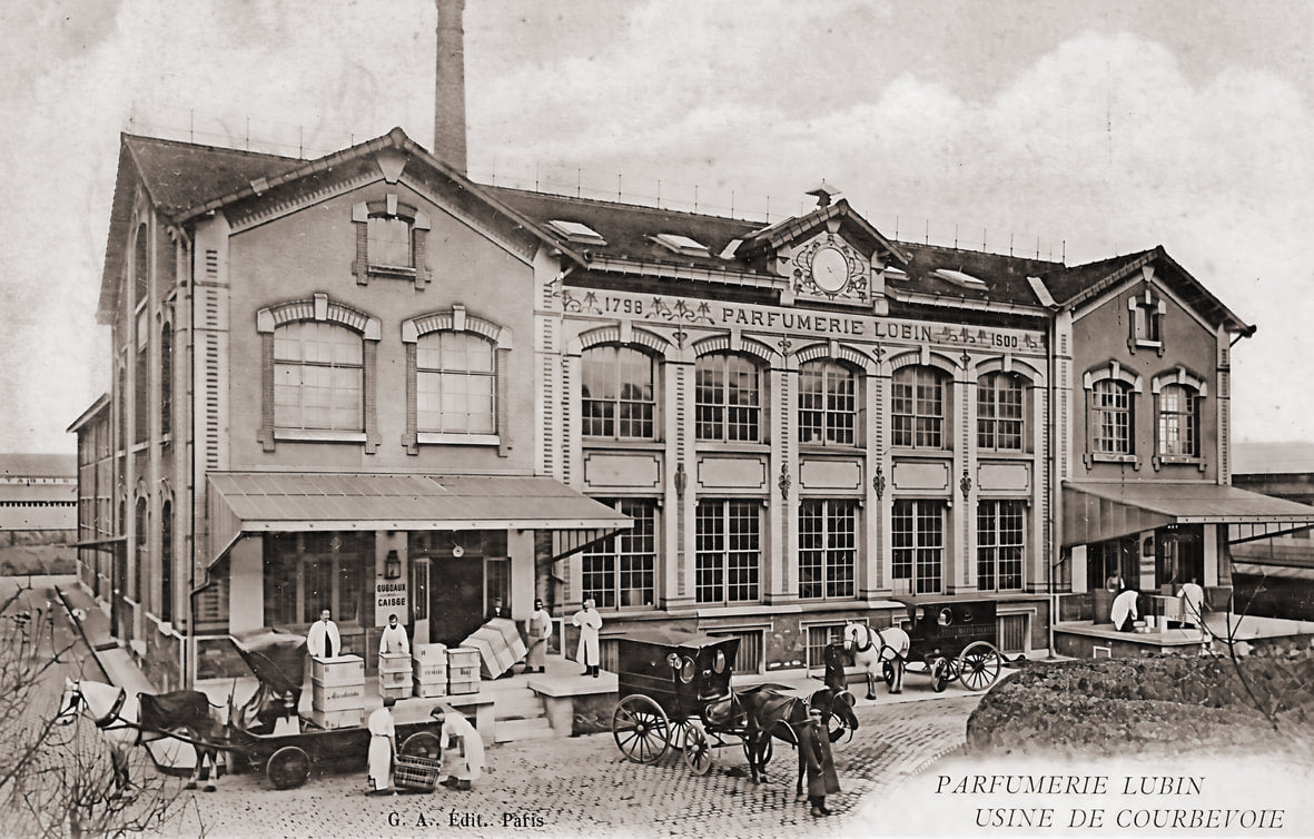 Carte postale ancienne de l'usine Lubin de Courbevoie : le bâtiment à deux niveaux porte l'enseigne « Parfumerie Lubin » sur sa façade, une haute cheminée s'élève à l'arrière et des attelages chargés de caisses stationnent devant l'entrée.